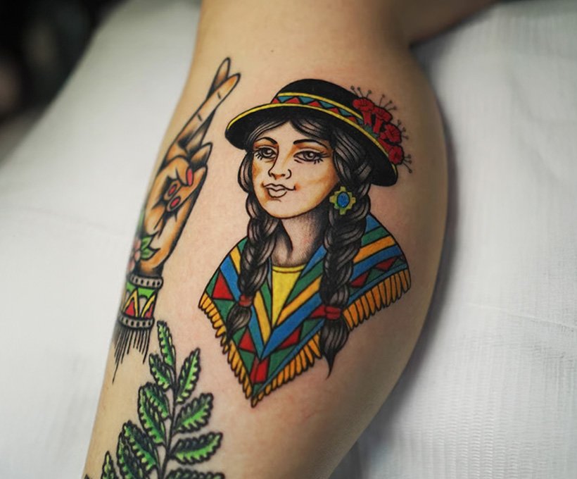 Traditional tattoo of a Cusqueña woman wearing a colorful Andean poncho and hat with kantuta flowers, created at NOIR Tattoo Studio in Cusco, Peru.