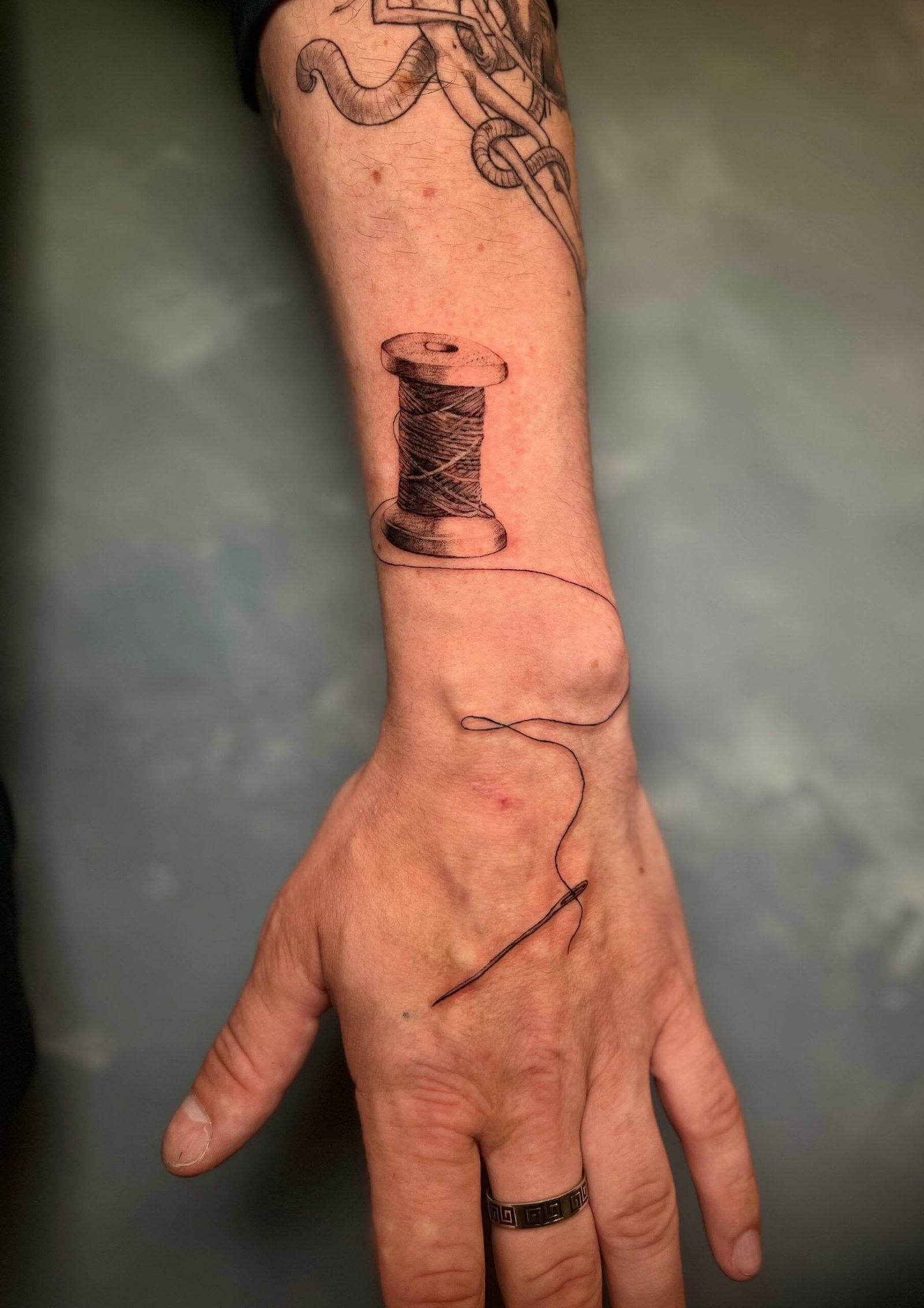 Realistic black and grey tattoo of a woman's face with a single tear and a hand holding a mask, created at NOIR Tattoo Studio in Cusco, Peru.