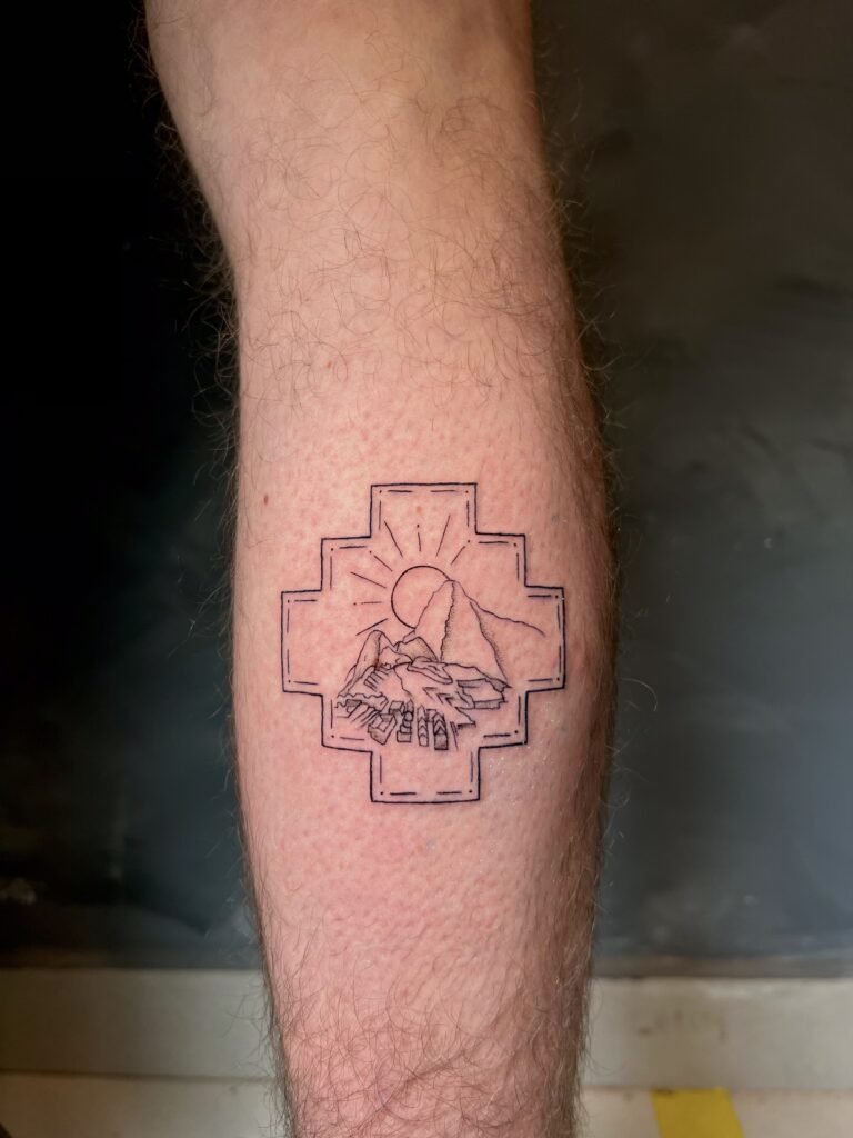 Fine line tattoo of a Chakana, the Andean cross, featuring Machu Picchu and the rising sun, symbolizing balance, connection, and spiritual energy, created at NOIR Tattoo Studio in Cusco, Peru.