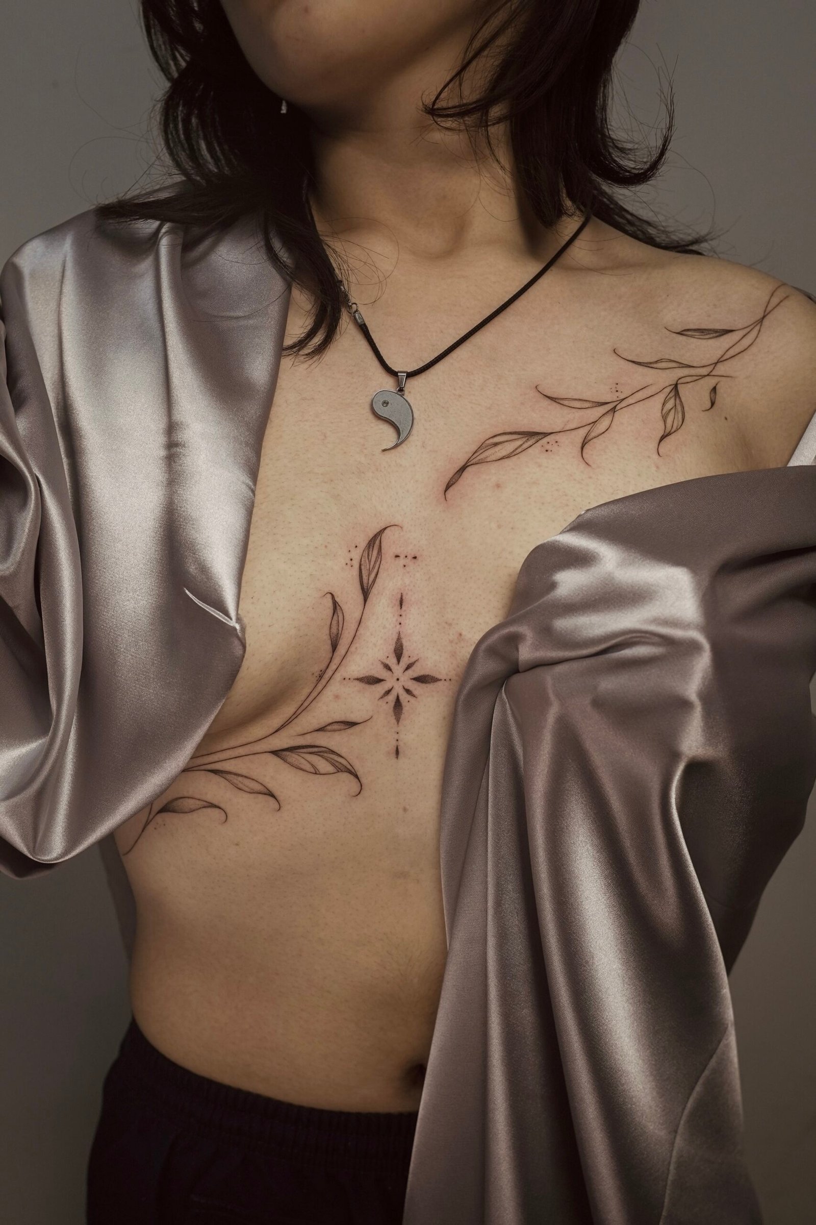 Delicate fineline ornamental tattoo on the chest featuring flowing botanical lines and a sacred star symbol, representing balance, femininity, and spiritual energy. Created at NOIR Tattoo Cusco, Peru.