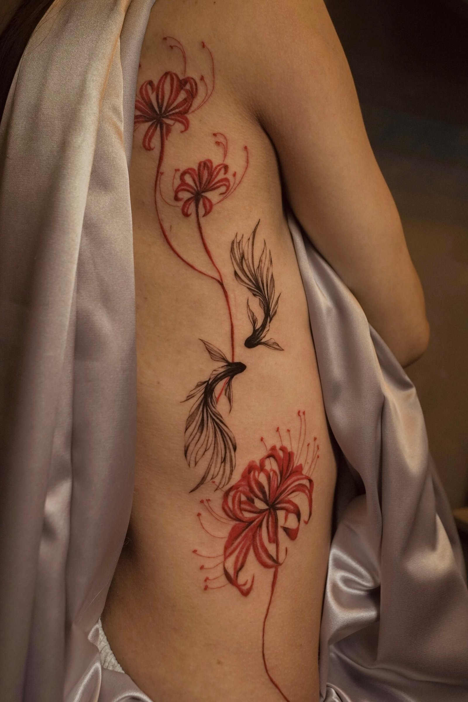 Elegant fineline tattoo featuring red Lycoris flowers and flying birds along the side of the body, symbolizing transformation, farewell, and spiritual rebirth. Created at NOIR Tattoo Cusco, Peru.