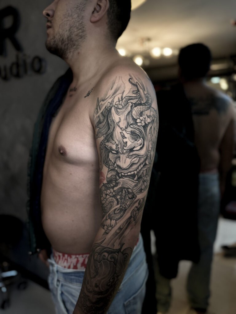 Black and grey Japanese sleeve tattoo featuring a detailed Hannya mask, symbolizing emotional duality, protection, and strength — healed piece created at NOIR Tattoo Cusco, Peru.