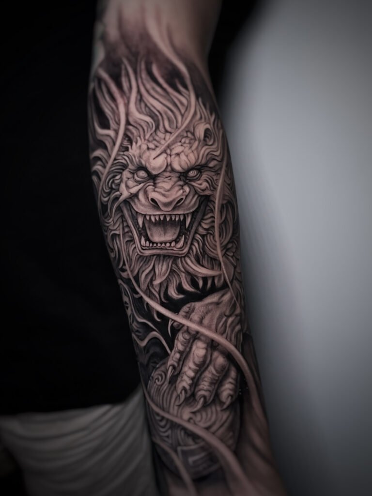Black and grey realism tattoo of a Japanese lion guardian (Shishi) with flowing mane and fierce expression, symbolizing protection, power, and spiritual strength. Created at NOIR Tattoo Cusco, Peru.