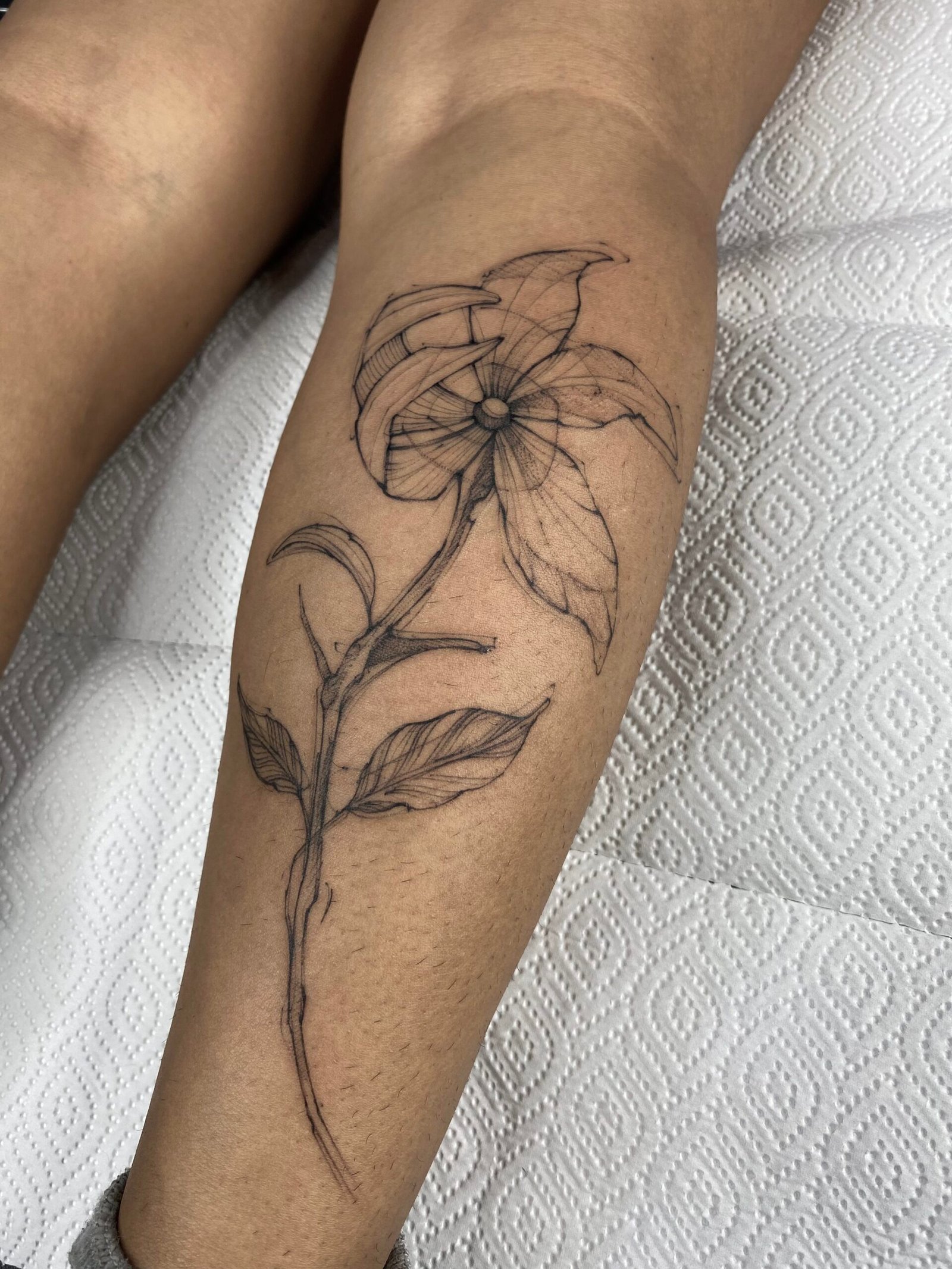 Realistic black and grey tattoo of a woman's face with a single tear and a hand holding a mask, created at NOIR Tattoo Studio in Cusco, Peru.