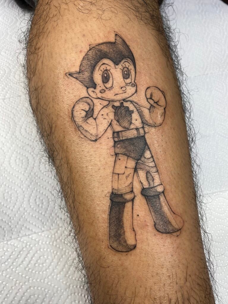 Black and grey tattoo of Astro Boy on the leg, featuring clean shading and classic anime design — crafted at NOIR Tattoo Cusco, Peru.