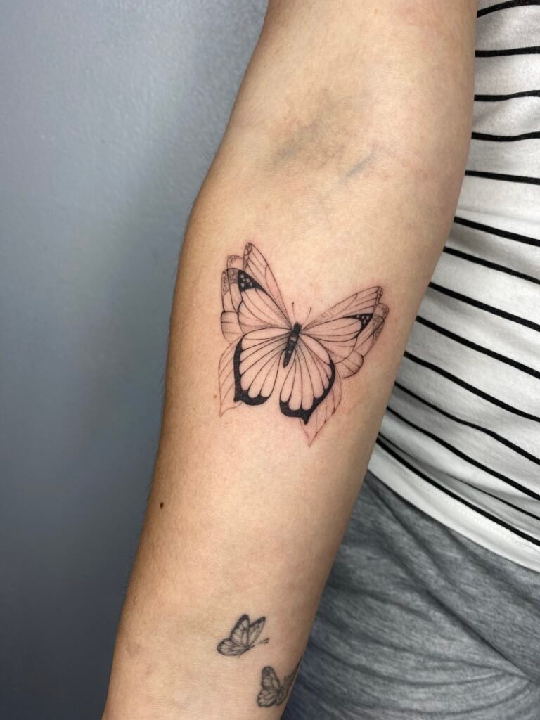 Delicate butterfly sketch tattoo with soft red and black lines on the forearm, symbolizing transformation and freedom. Created at NOIR Tattoo Cusco, Peru.