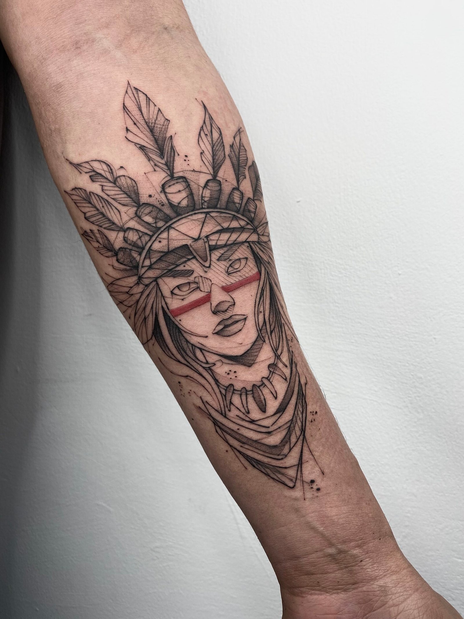Fineline tattoo of an Andean warrior woman with feathers and red facial markings, symbolizing strength and ancestral identity. Created at NOIR Tattoo Cusco, Peru.