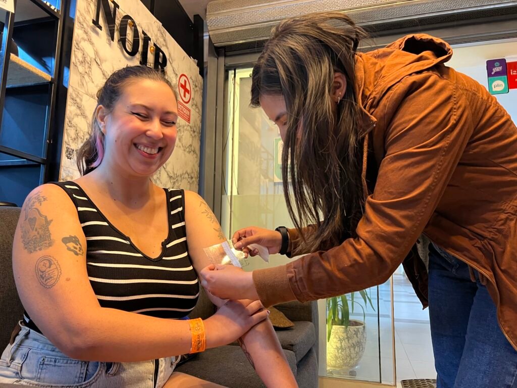 Tattoo artist from NOIR Tattoo Cusco sharing a joyful moment with an American client after finishing a tattoo, highlighting connection and artistic experience in Cusco, Peru.
