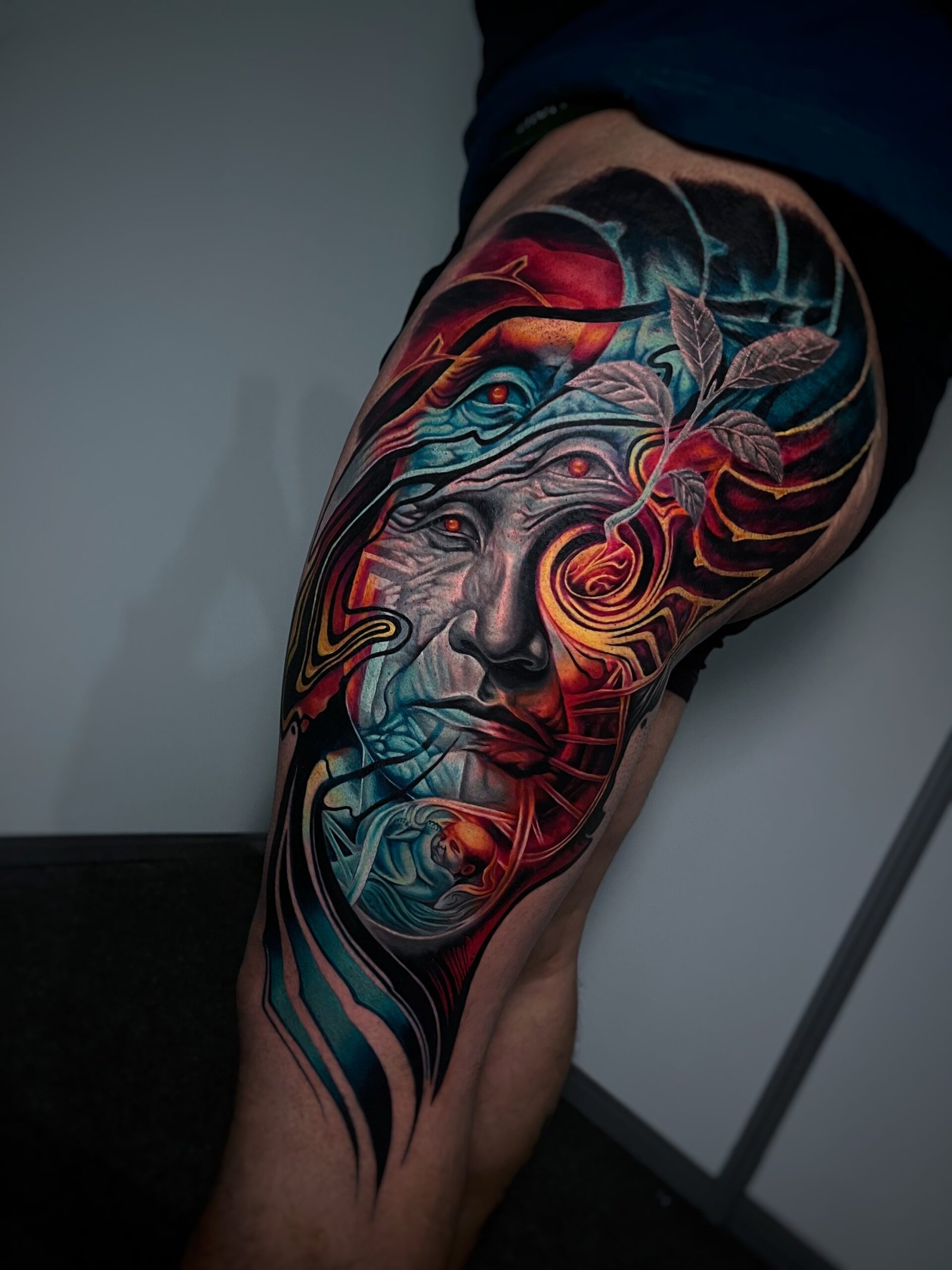 Realistic black and grey tattoo of a woman's face with a single tear and a hand holding a mask, created at NOIR Tattoo Studio in Cusco, Peru.