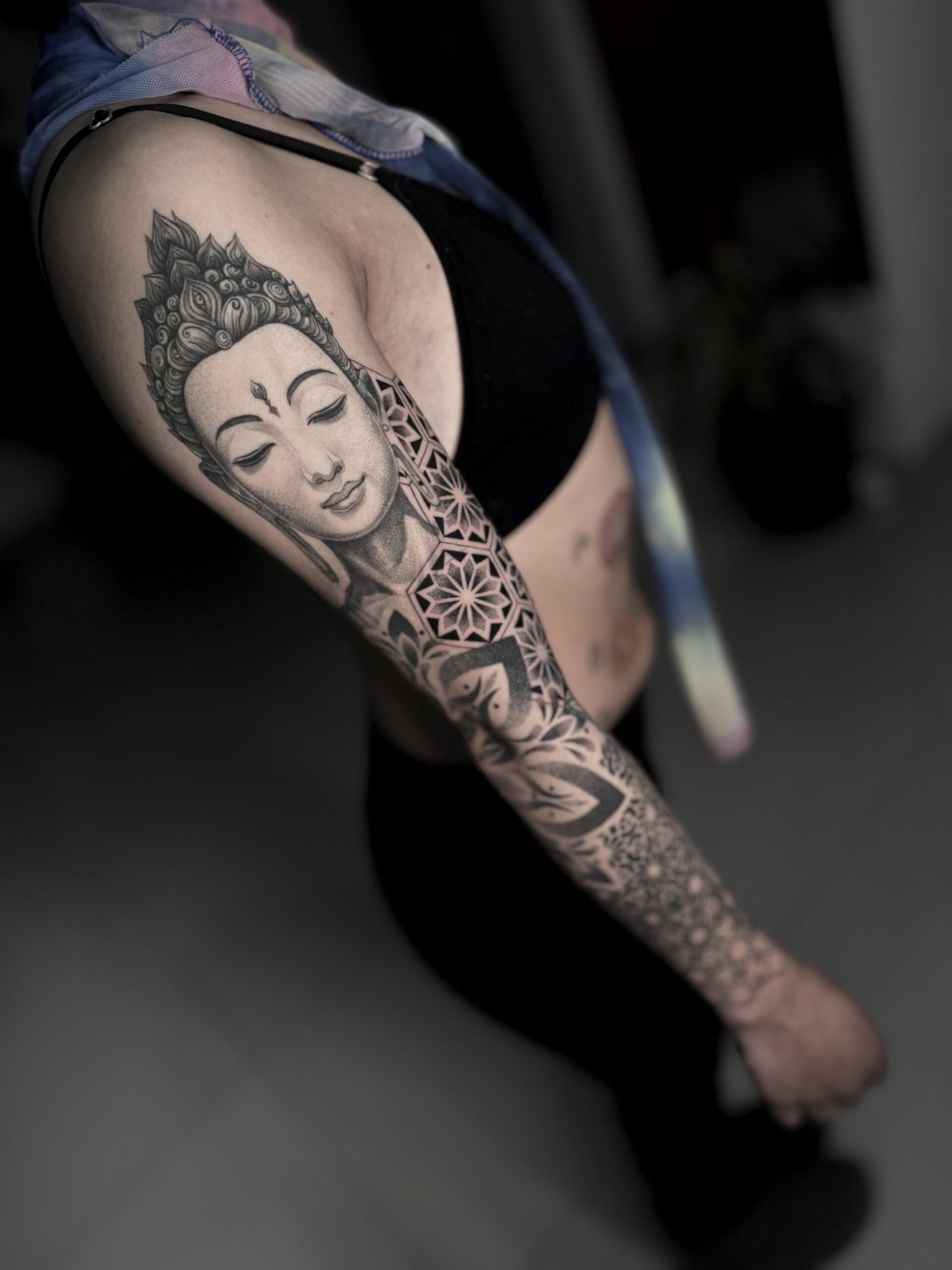 Black and grey Buddha sleeve tattoo with mandala, lotus, and sacred geometry dotwork on a woman’s arm, symbolizing peace, mindfulness, and spiritual protection — NOIR Tattoo Cusco.