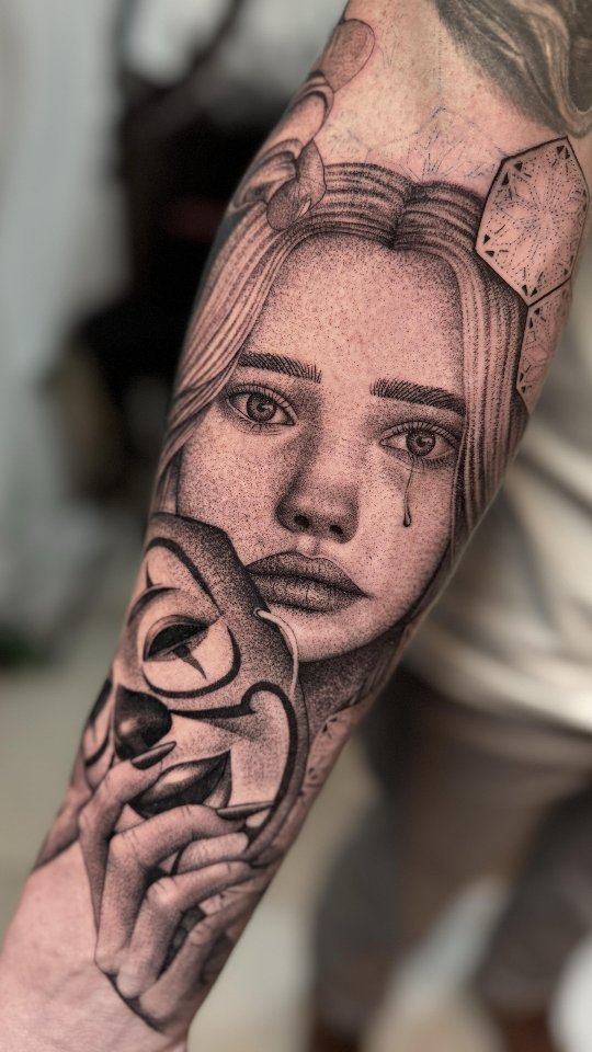 Realistic black and grey tattoo of a woman's face with a single tear and a hand holding a mask, created at NOIR Tattoo Studio in Cusco, Peru.