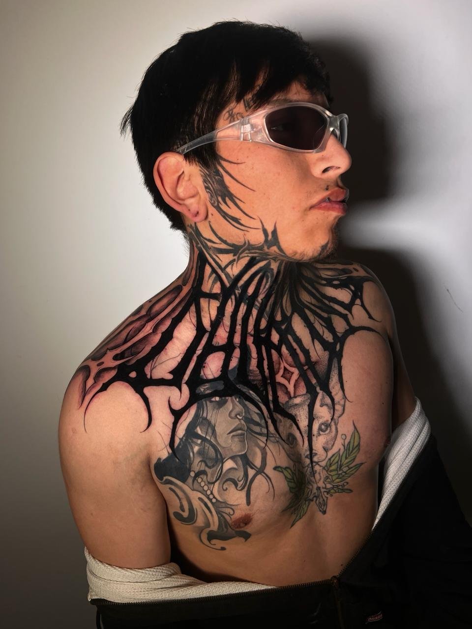 Black and grey chest tattoo of an ayahuasca vine (Banisteriopsis caapi) with leaves and flower intertwined with an Andean geometric sun/mandala, symbolizing healing, vision, and protection — created at NOIR Tattoo Cusco, Peru.