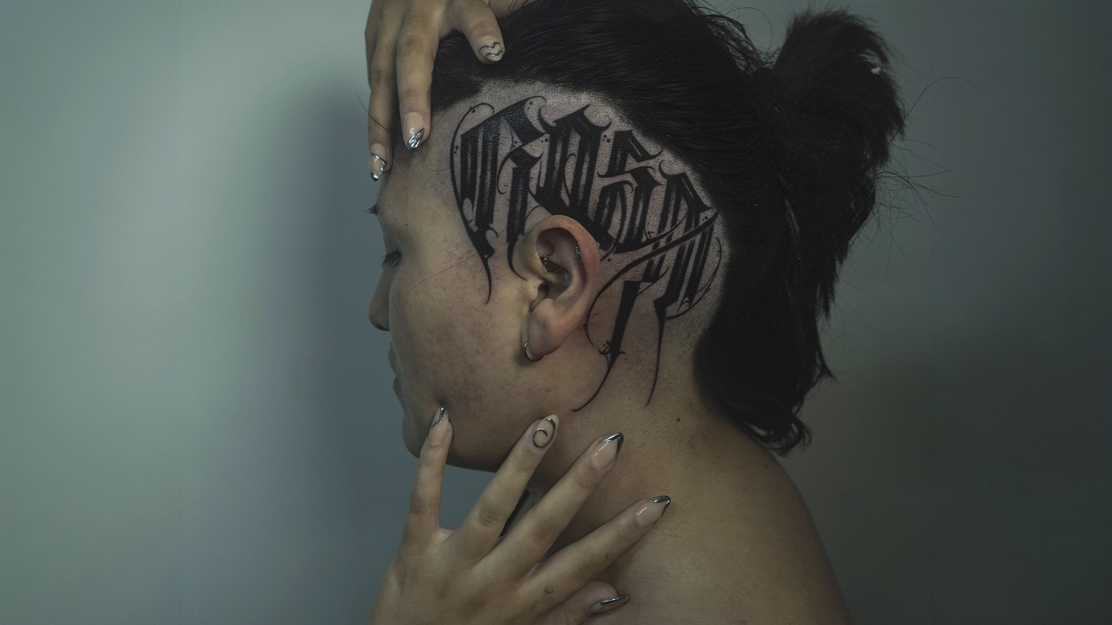 Custom blackwork calligraphy scalp tattoo with gothic lettering on the side of the head, tattooed at Noir Tattoo Cusco, Peru.