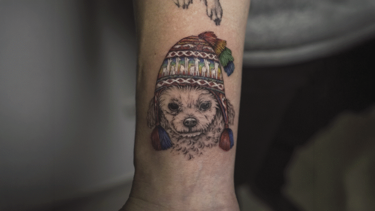 Cute dog portrait tattoo wearing a traditional Andean chullo hat, created in black and grey with colorful details at Noir Tattoo Cusco, Peru.