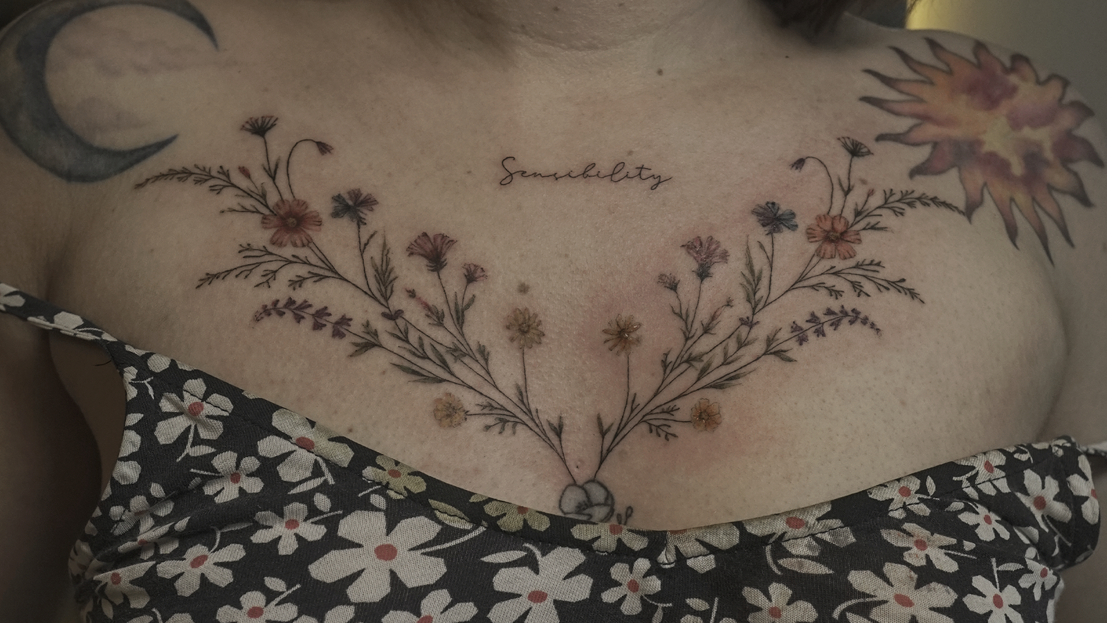 Delicate fine line wildflower chest tattoo with colorful botanical flowers, created at Noir Tattoo Cusco, Peru.
