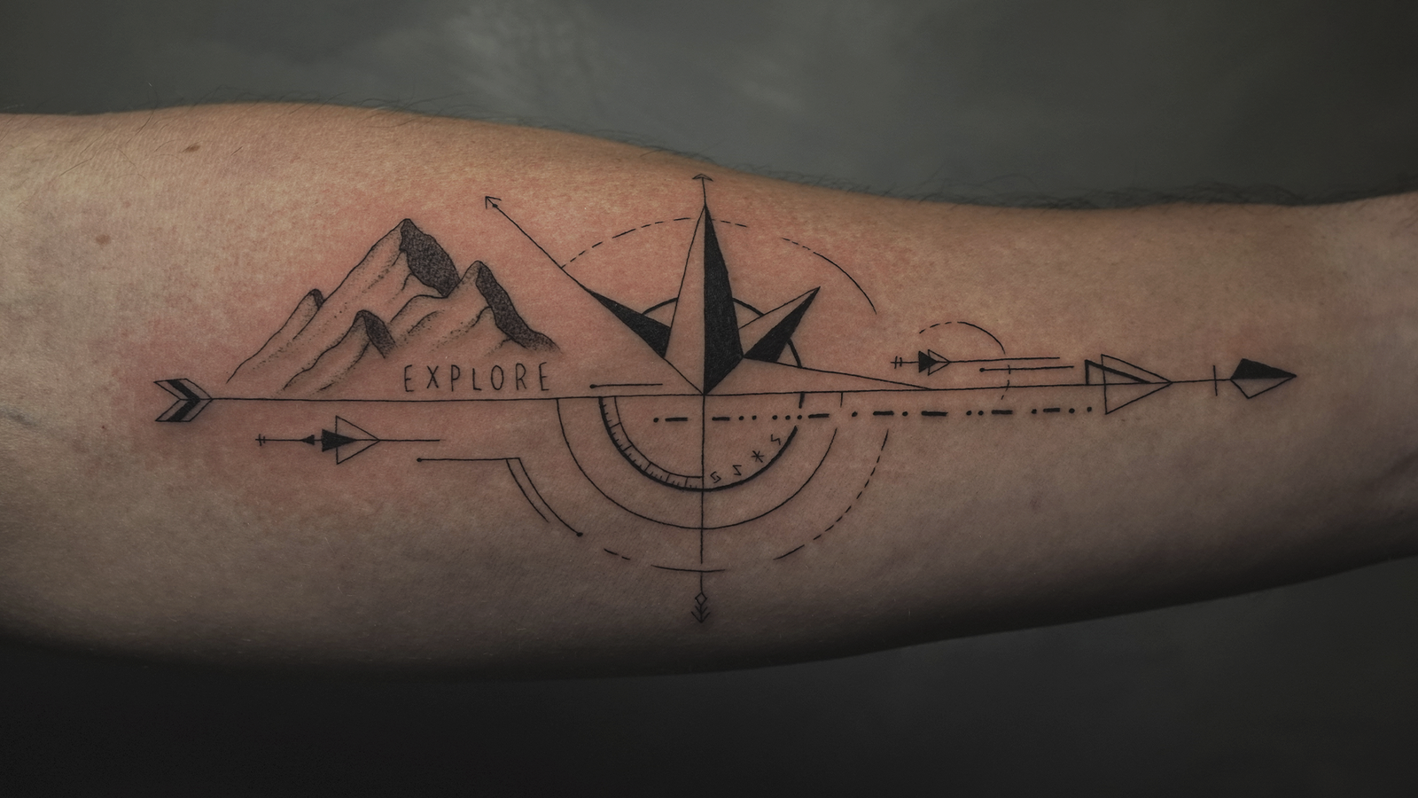 Geometric compass and mountain tattoo on the forearm with the word "Explore," symbolizing adventure, travel, and direction.