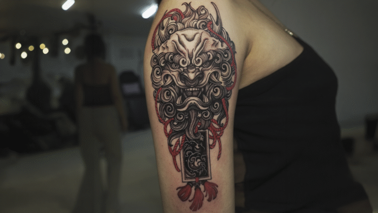 Japanese Foo Dog tattoo in black and grey with red accents on the upper arm, symbolizing protection and strength.