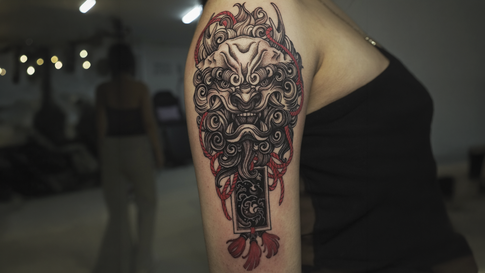 Japanese Foo Dog tattoo in black and grey with red accents on the upper arm, symbolizing protection and strength.