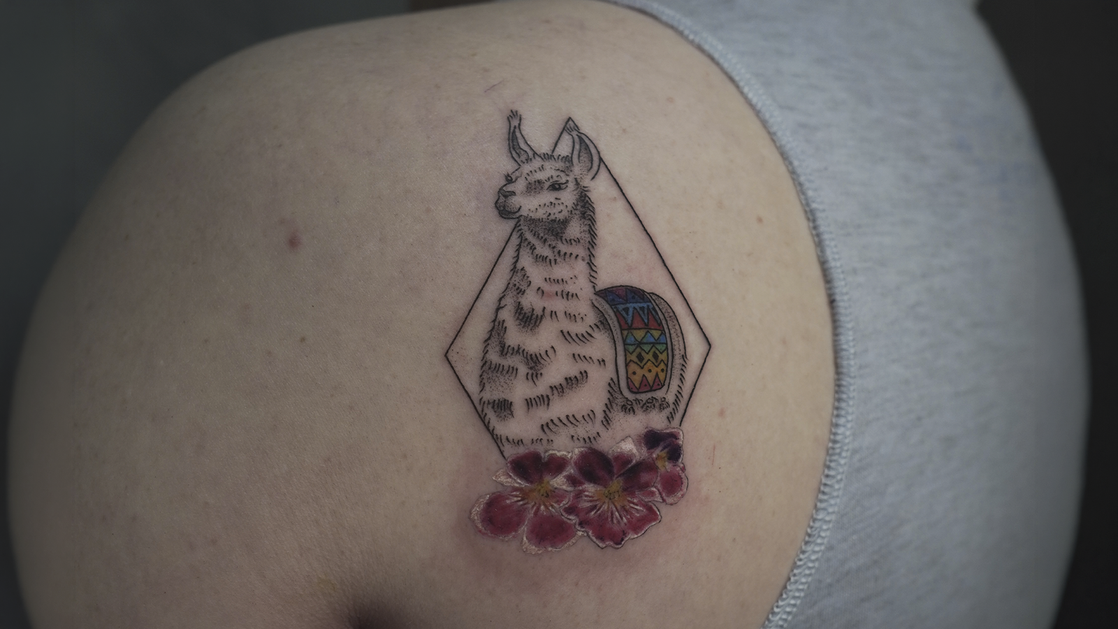 Fine line llama tattoo with colorful Andean textile details and flowers, inspired by Peruvian culture and created in Cusco, Peru.