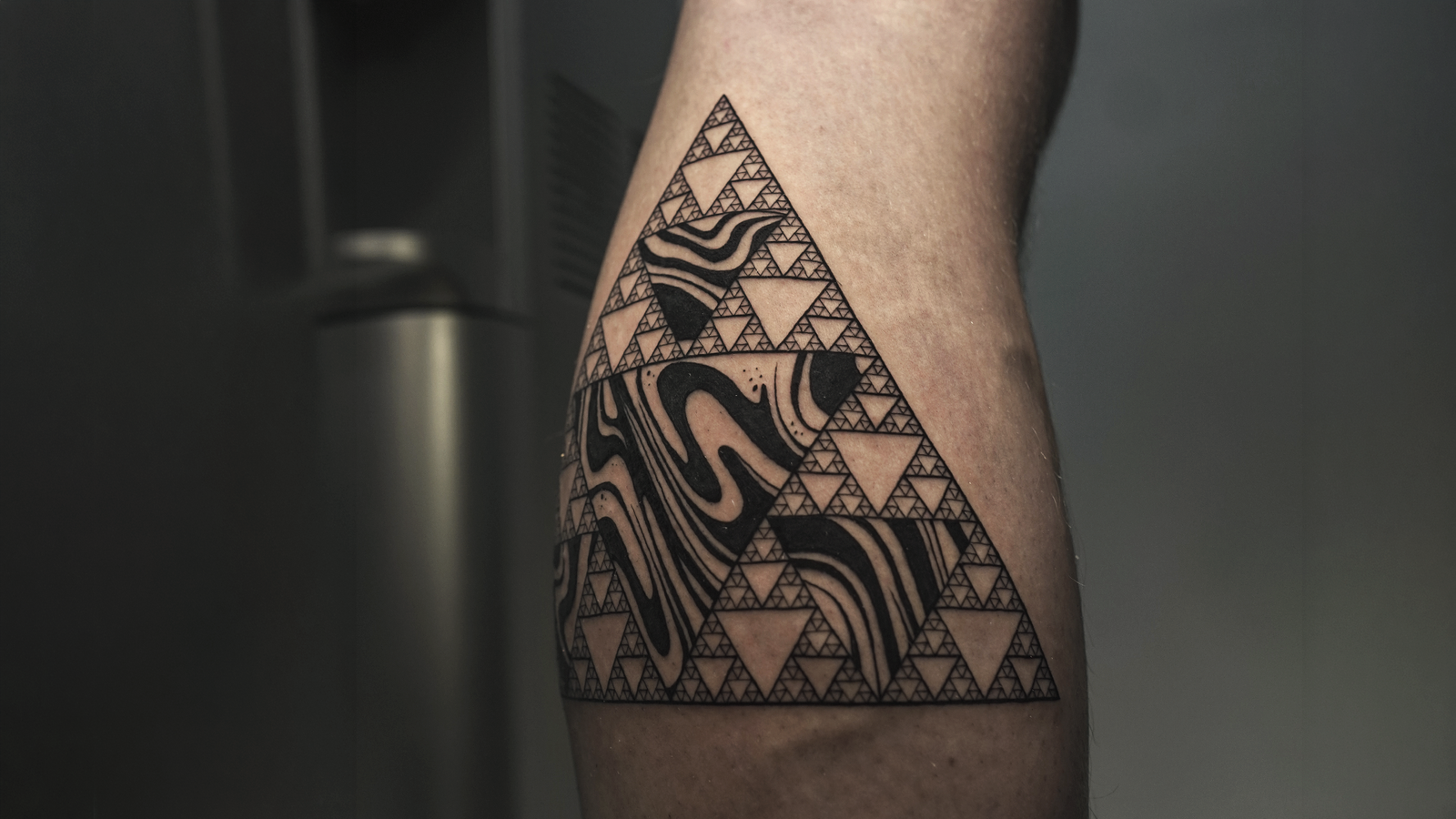 Geometric blackwork tattoo featuring a Sierpinski triangle fractal with abstract flowing patterns, created at Noir Tattoo Cusco, Peru.