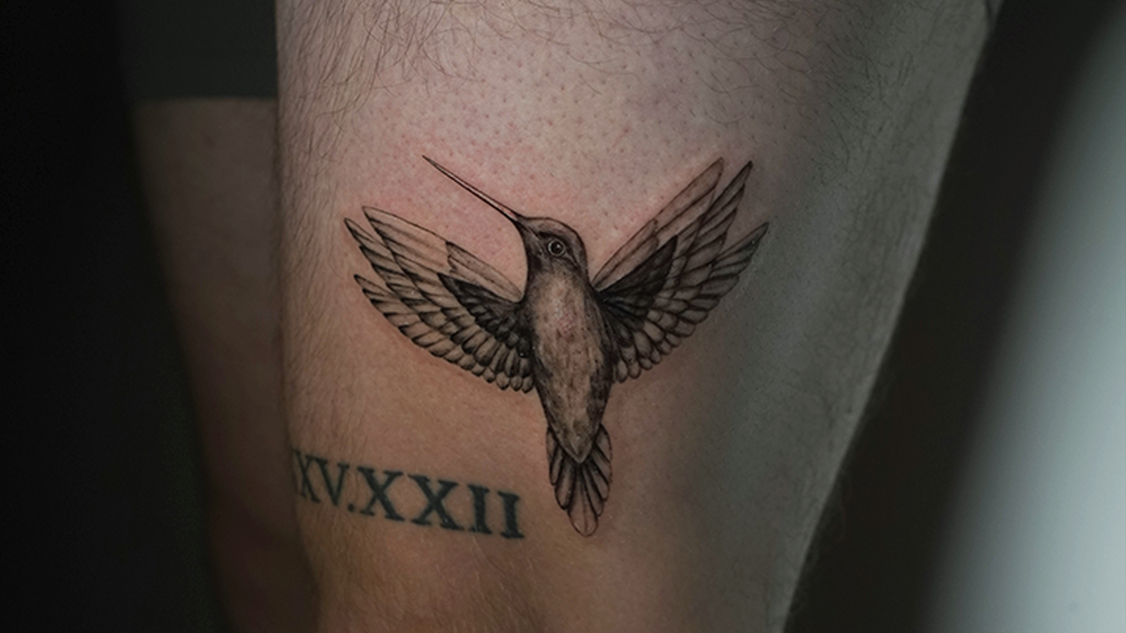 Black and grey realism hummingbird tattoo with wings spread in flight, created at Noir Tattoo Cusco, Peru.