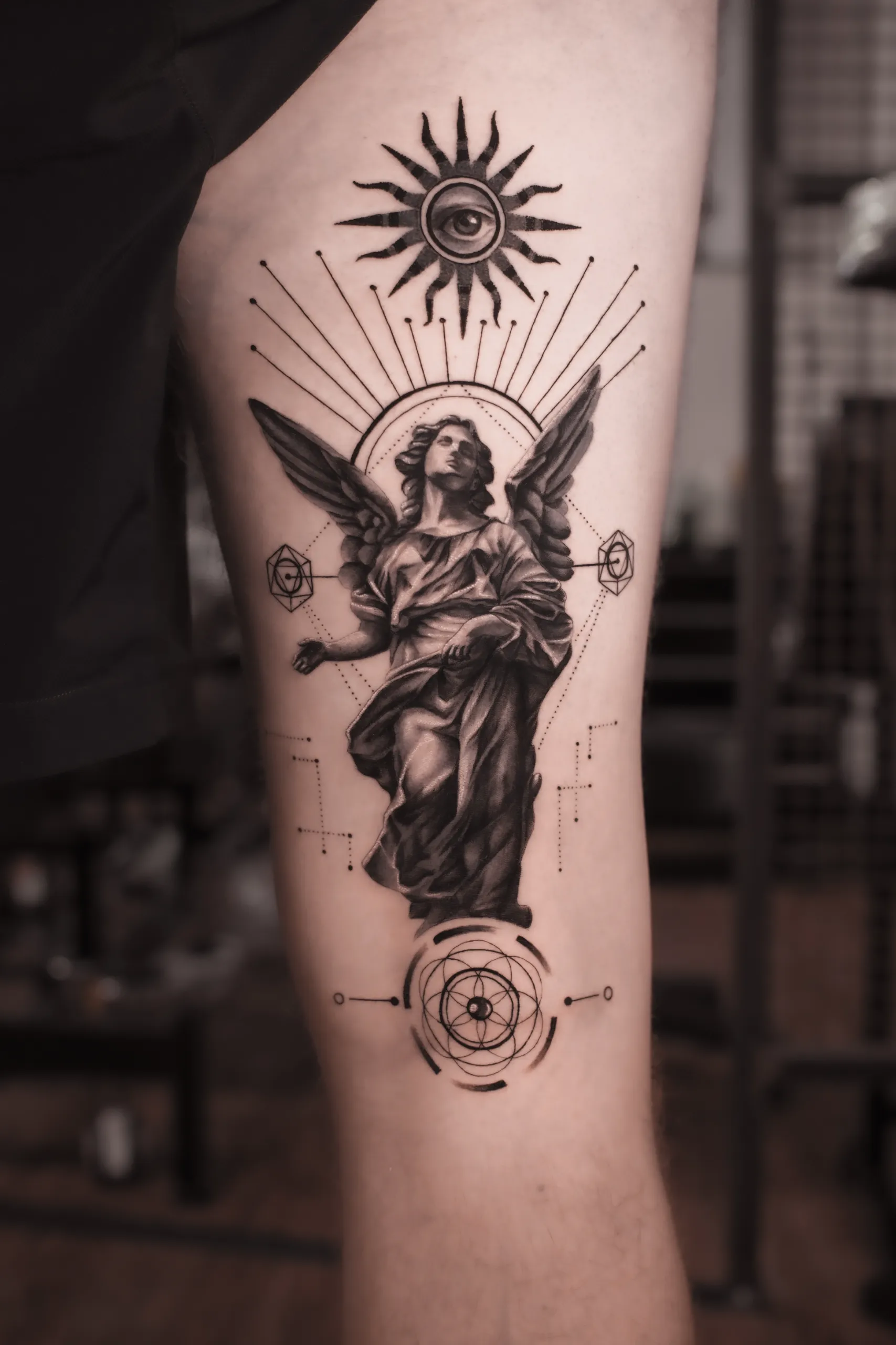 Black and grey angel tattoo with sacred geometry and all-seeing eye at Noir Tattoo Cusco