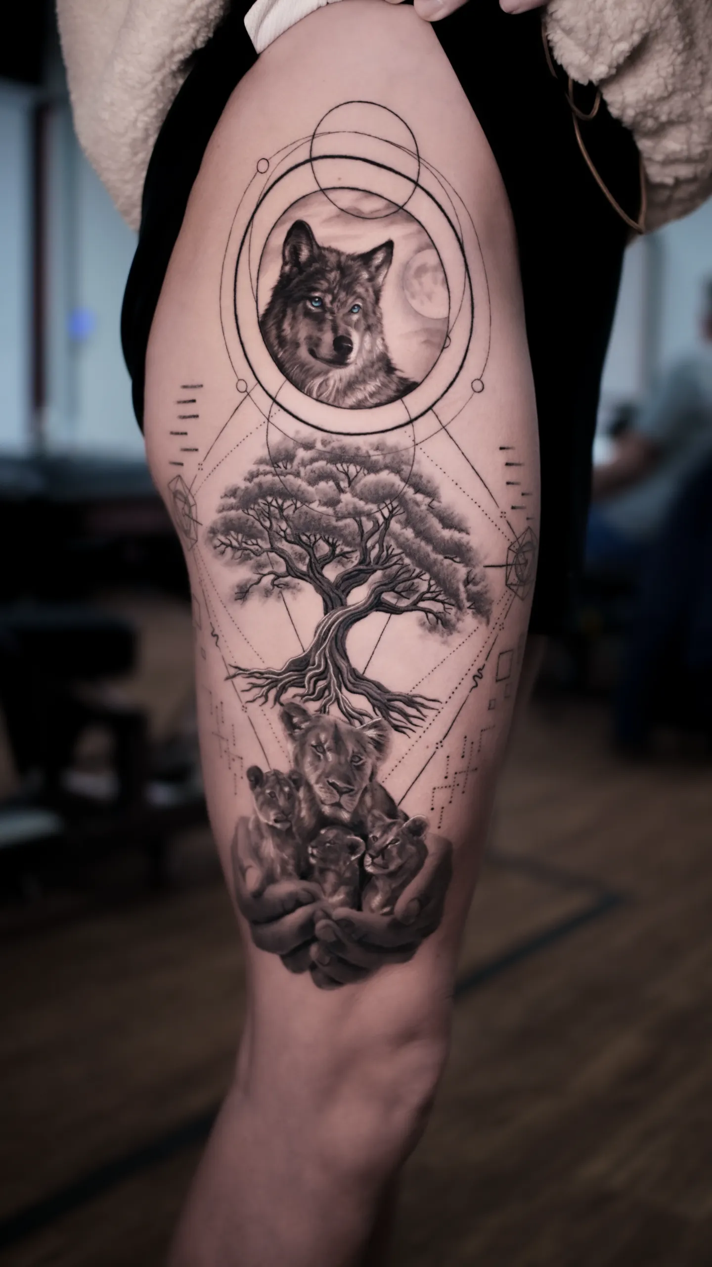 Black and grey wildlife tattoo with wolf, tree, lion family and geometric details at Noir Tattoo Cusco